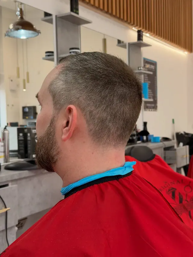 A short buzz cut with a trimmed beard, seen from behind, at a station with mirrors and shelves