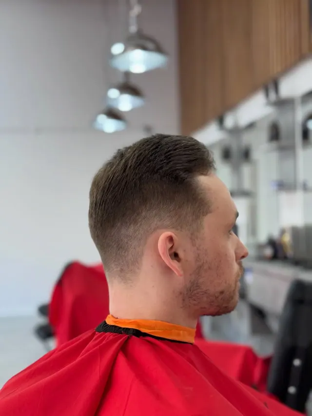 A short side-part cut seen from behind, under the shop's pendant lights