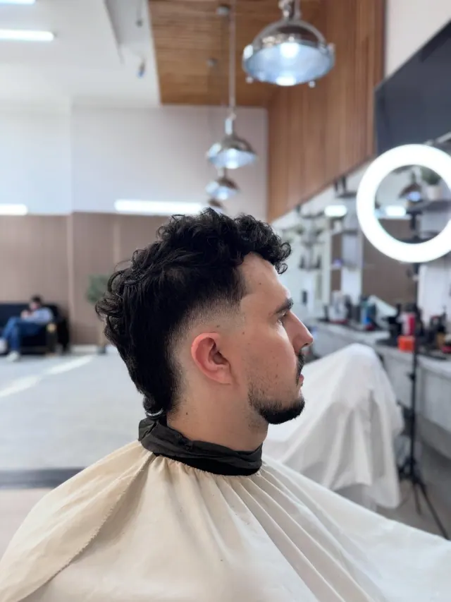 A curly cut with a skin fade at the back, under the pendant lights and ring light