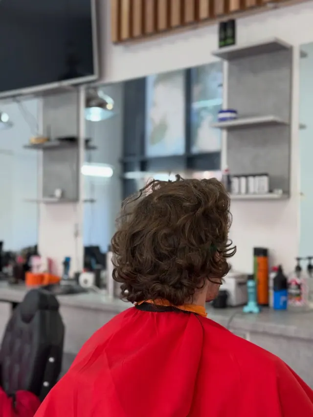 A curly cut from behind, facing the mirror and the shelves of products