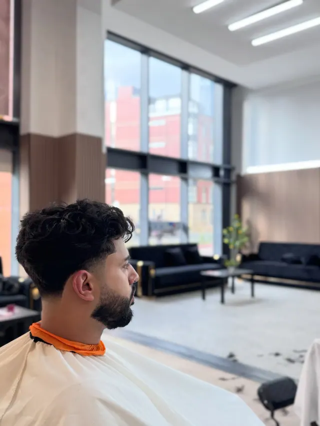 A curly textured crop with a fade, beside the tall windows and the waiting sofas